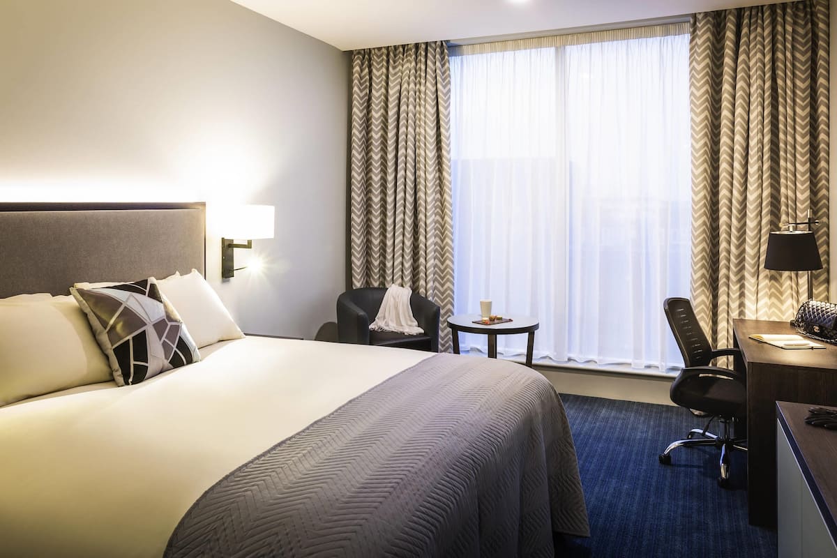 Een hotelkamer met een groot bed, een bureau, een stoel en een kleine tafel met een lamp.