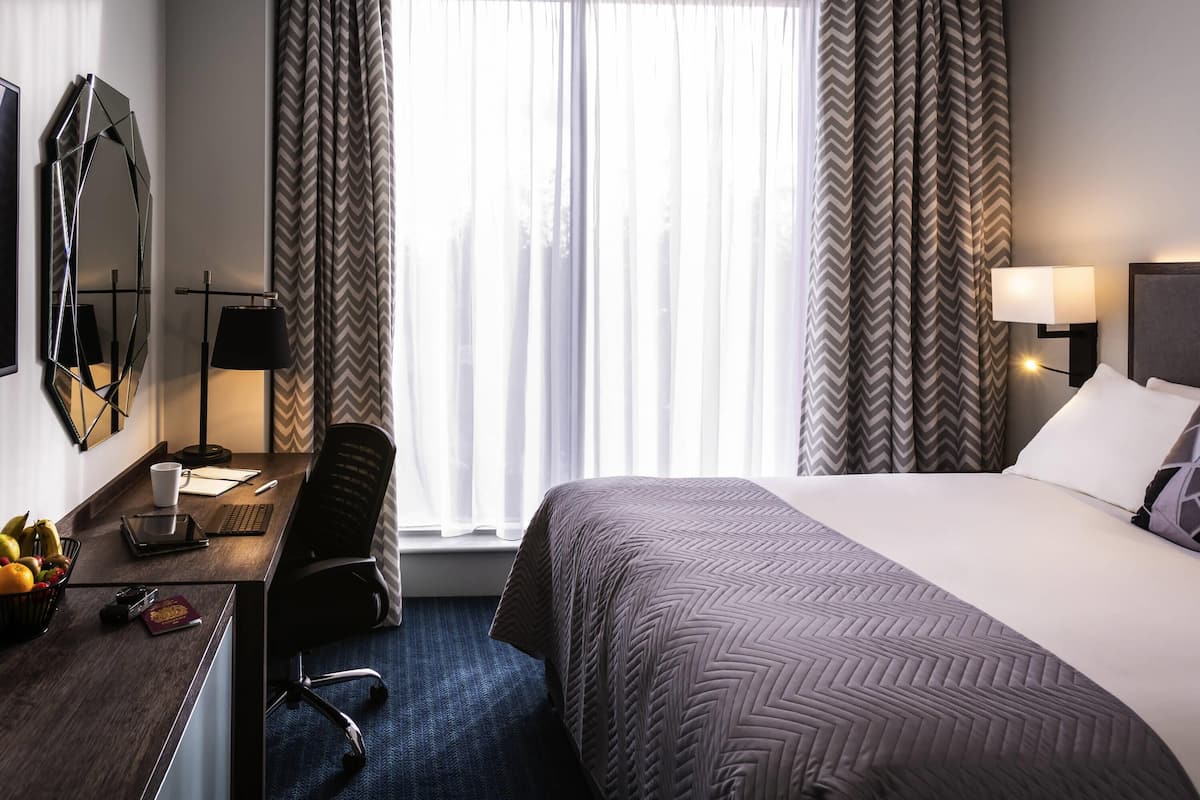 Een hotelkamer met een bed, bureau, stoel en een groot raam met gordijnen.