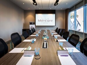 A conference room with a long table, chairs, a projector screen, and a banner for Mercure Hotels. - Mercure Bridgwater Hotel (Bridgwater)