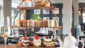 Une présentation de desserts en étages, avec des sandwichs, des gâteaux et une théière, sur une table dans un restaurant.