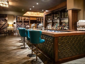 A bar area with a bar counter, stools, and a variety of bottles.