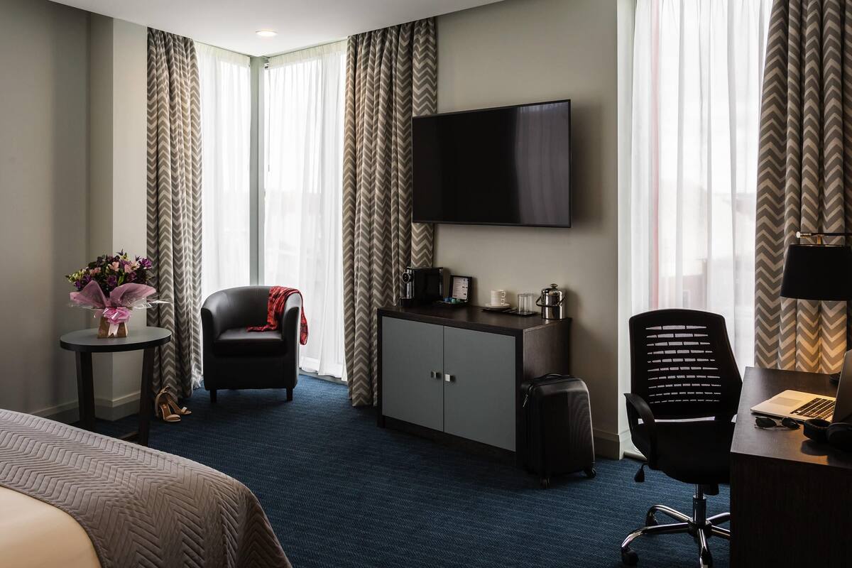 Hotelkamer met een bed, een bureau met een laptop, een stoel, een televisie, een koffiezetapparaat en een koffer.