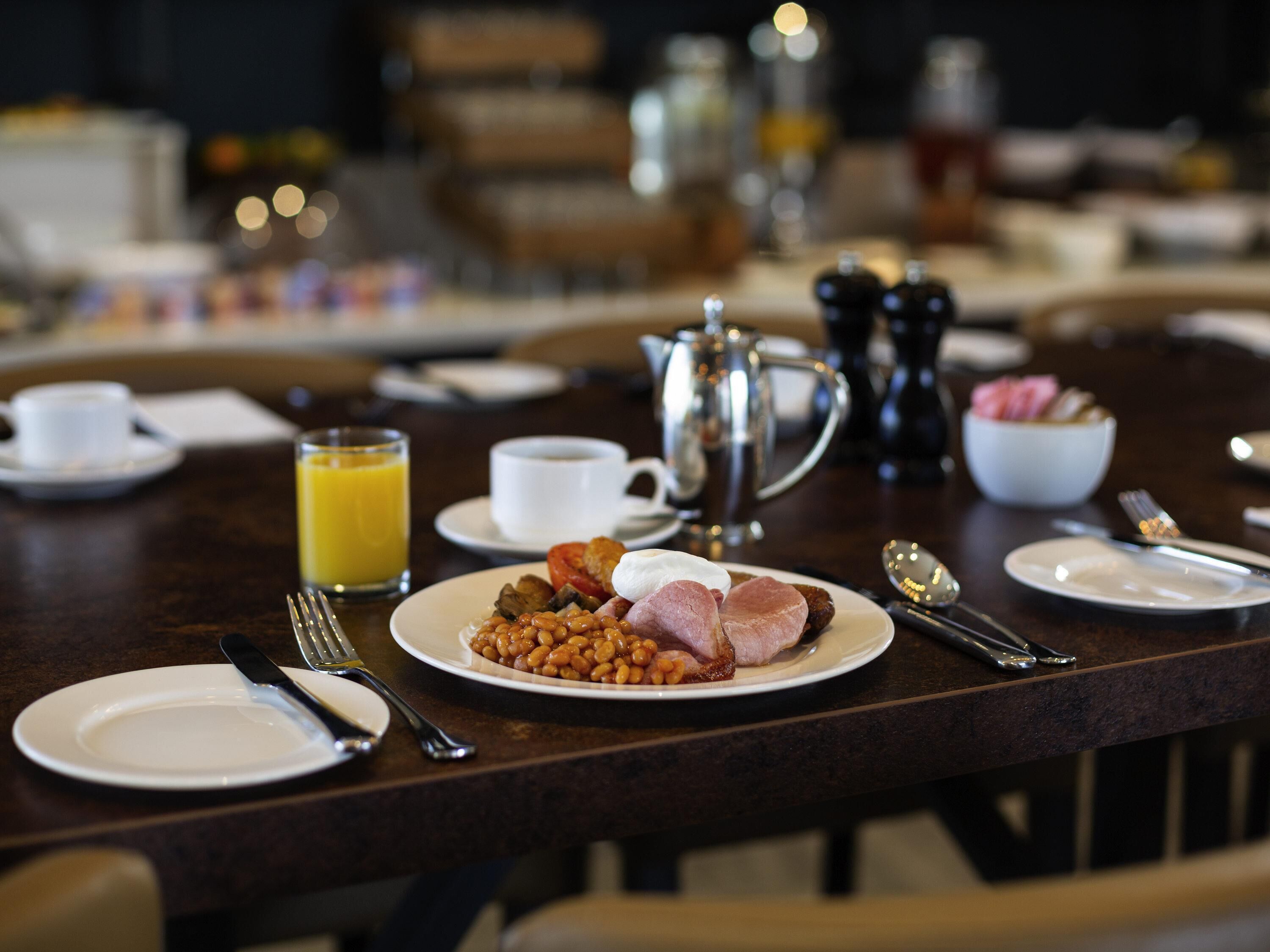 A breakfast table set with plates, cutlery, a coffee pot, and a jug of orange juice.