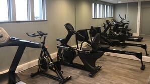 Une salle de sport équipée de vélos d’appartement, de tapis de course et d’un mur recouvert de miroirs.