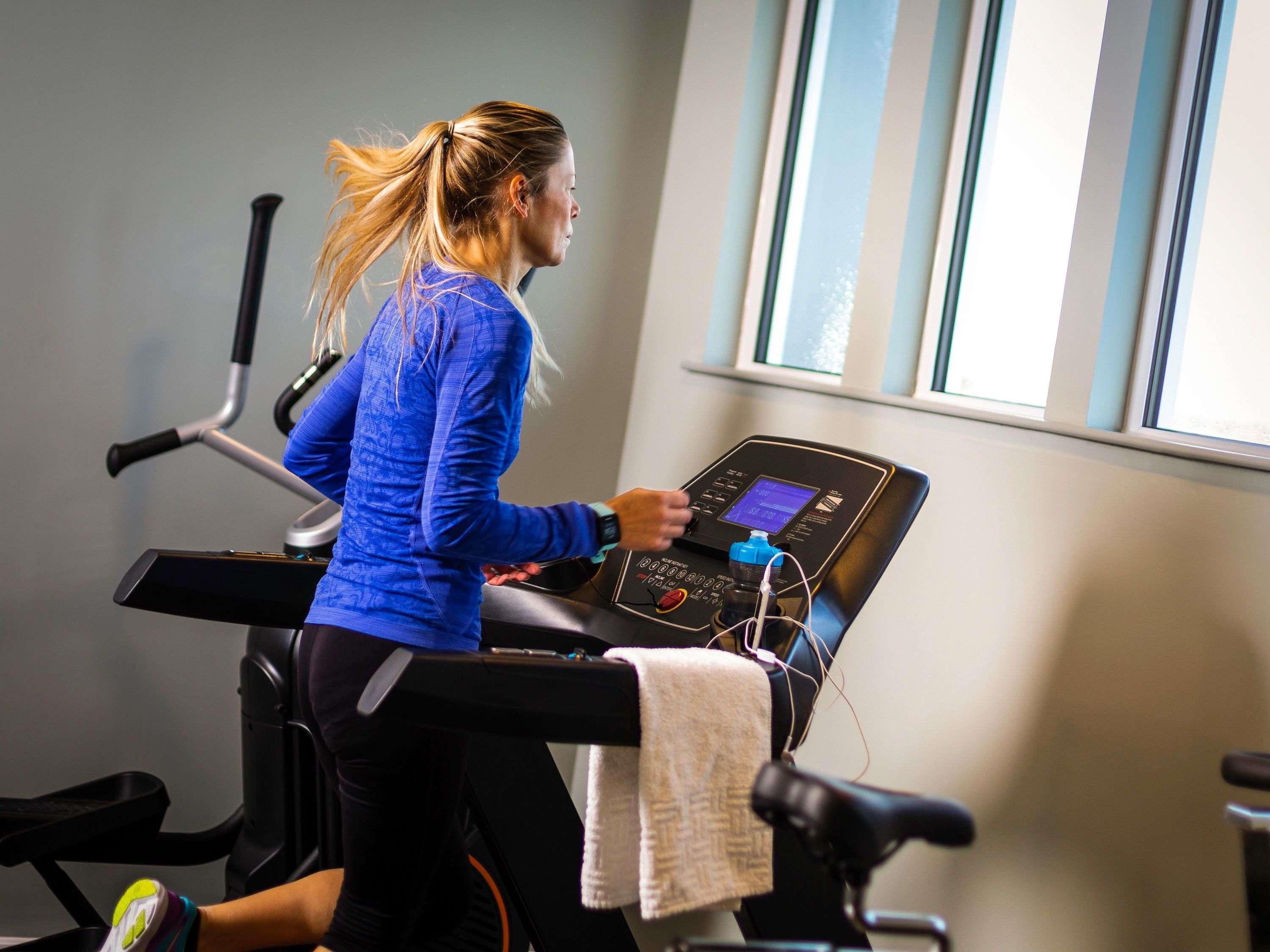 A person using a stationary bike in a gym with a window and exercise equipment in the background.