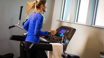 A person using a stationary bike in a gym with a window and exercise equipment in the background.