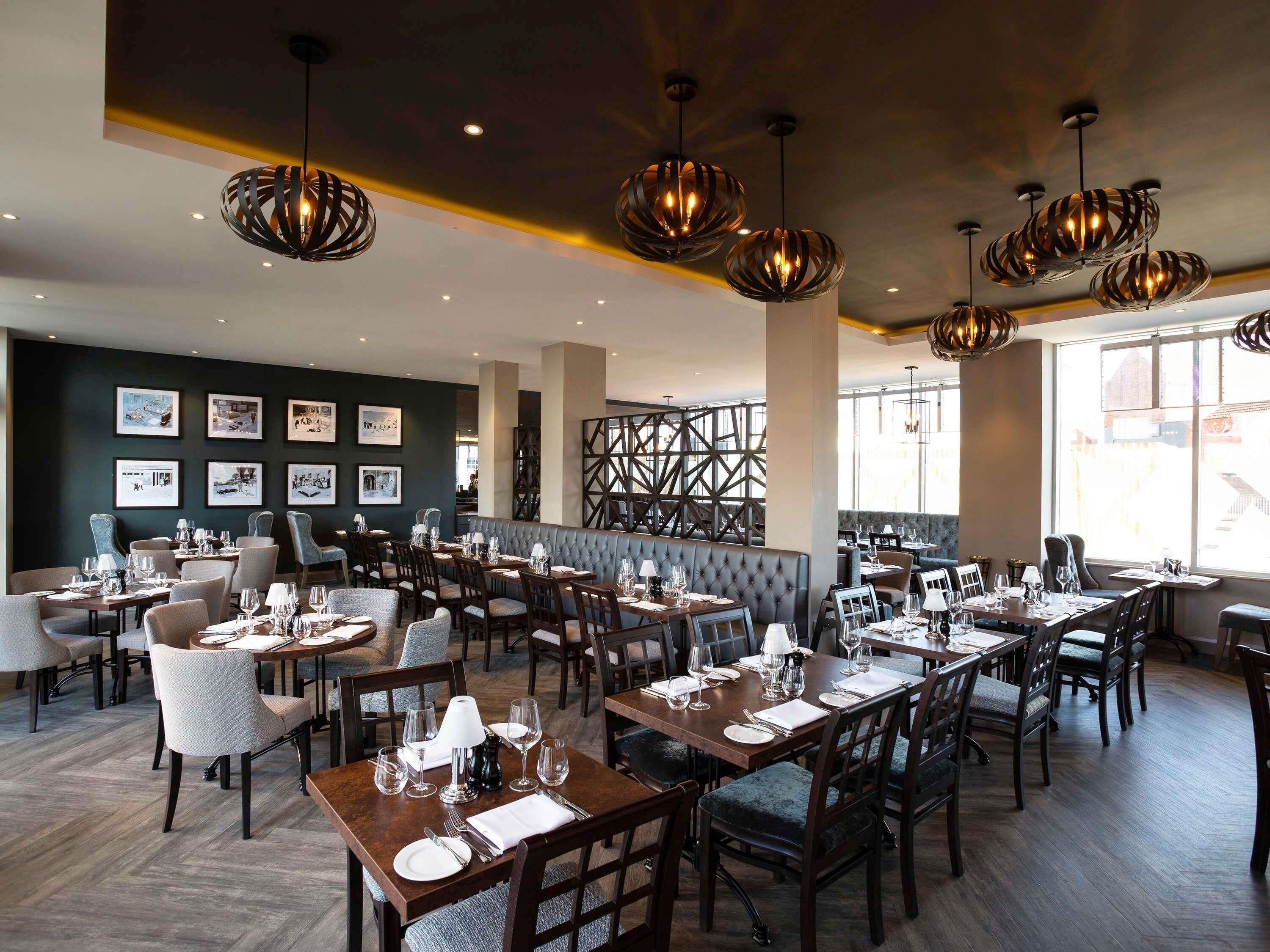 A restaurant with multiple dining tables, chairs, and hanging pendant lights.