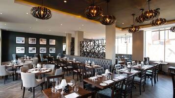 A restaurant with multiple dining tables, chairs, and hanging pendant lights.