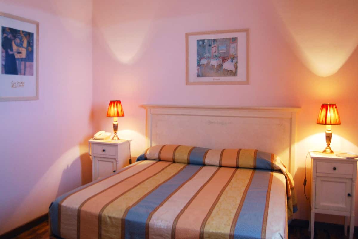 A hotel room with a bed, two bedside tables, a nightstand, a lamp, and two framed pictures on the walls.