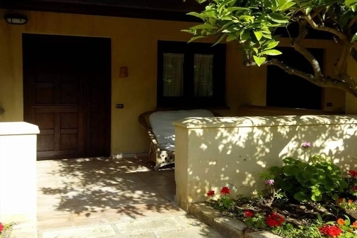 A courtyard with a bed, a door, and a wall with a flower bed.