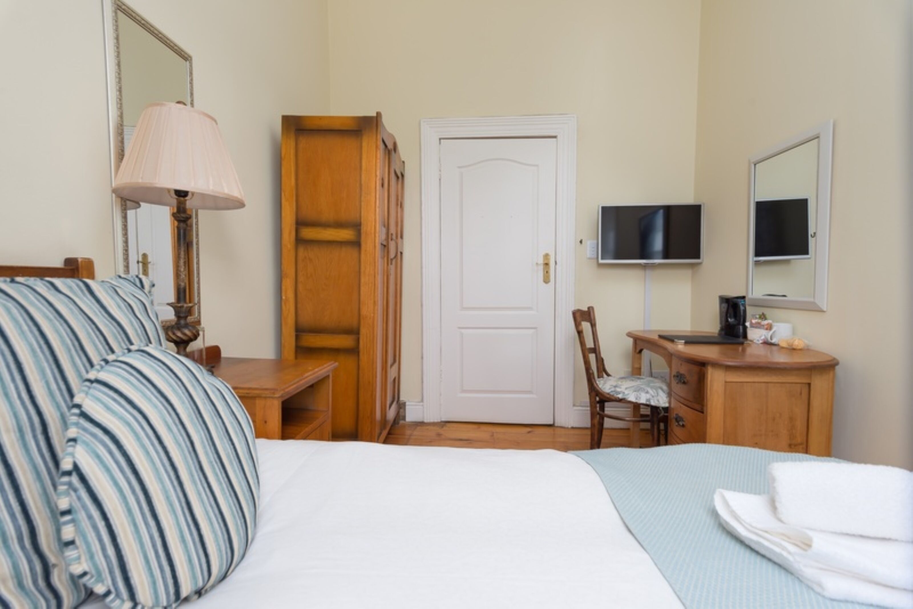 A hotel room with a bed, a desk, a chair, a television, and a door.