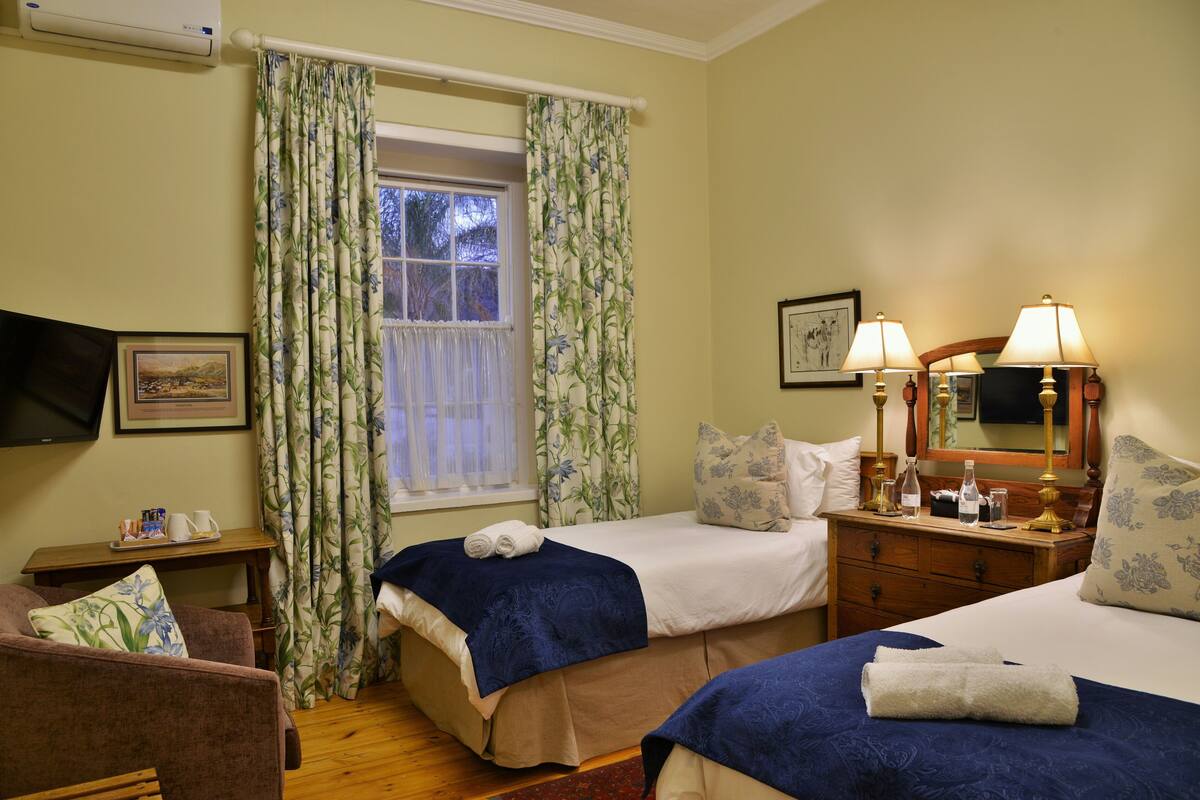 Habitación de hotel con dos camas, una televisión, una mesita de noche con lámparas y una ventana con cortinas.