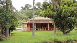 A red building with a tiled roof, surrounded by lush greenery and a small pond. - Pousada Gruta do Anjo (Socorro)