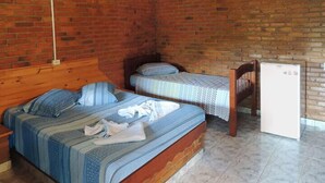 A room with a brick wall, a wooden bed, a small table, and a white refrigerator. - Pousada Gruta do Anjo (Socorro)