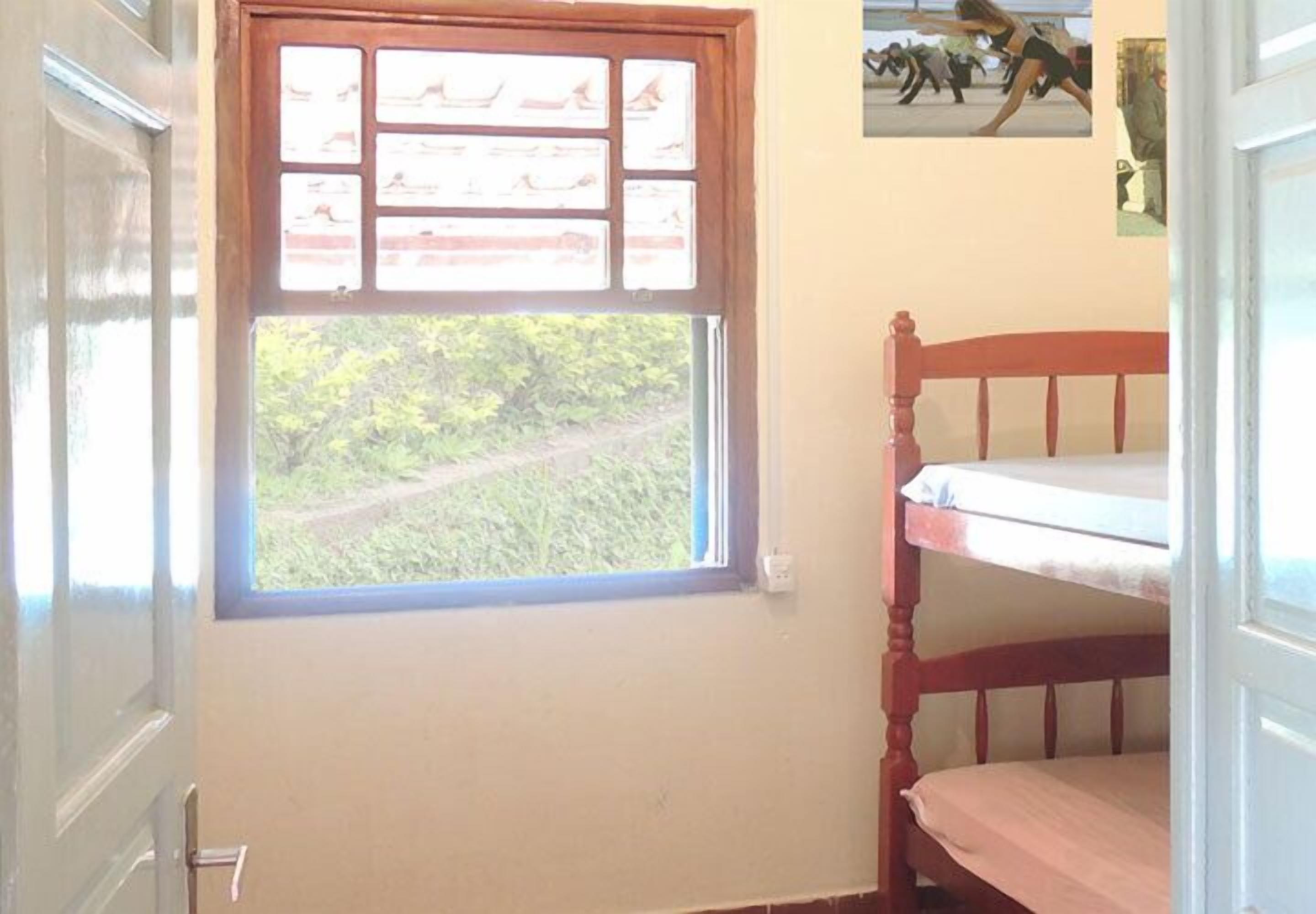 A room with a bunk bed, a window with a view of greenery, and a wall with informational posters.
