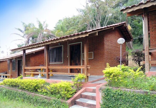 A rustic wooden cabin with a porch, steps leading to the entrance, and a satellite dish on the roof.