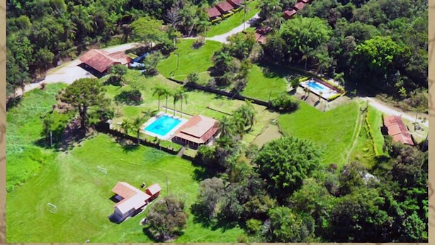 An aerial view of a resort with multiple bungalow-style buildings, a central swimming pool, and well-maintained lawns. - Pousada Gruta do Anjo (Socorro)