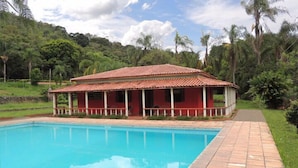 A swimming pool with a red-roofed building in the background. - Pousada Gruta do Anjo (Socorro)