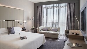 Una habitación de hotel moderna con una cama grande, un sofá, un escritorio y un ventanal con cortinas.