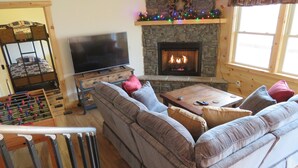 A cozy living room with a sectional sofa, a flat-screen TV, a fireplace, and a foosball table. - Secluded mountain cabin 5 acres , all rooms with view,  hear soothing waterfall (Maggie Valley)