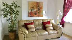 A beige leather sofa with red and patterned cushions, a large potted plant, and a painting on the wall. -  Minutes from Downtown, Pittsburgh’s international airport,  & Sports’ arenas! (Pittsburgh)