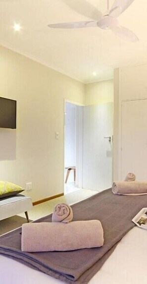 A modern hotel room with a ceiling fan, a bed with a grey mattress, and two rolled towels on the floor. - Afribode Monreith Apartment (Cape Town)