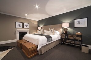 A bedroom with a bed, a dresser, a nightstand, a lamp, and a fireplace.