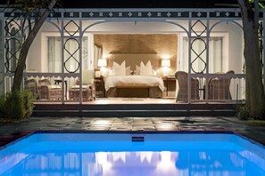 A bedroom with a large bed, two bedside lamps, and wicker furniture. - The Milner (Makhanda)