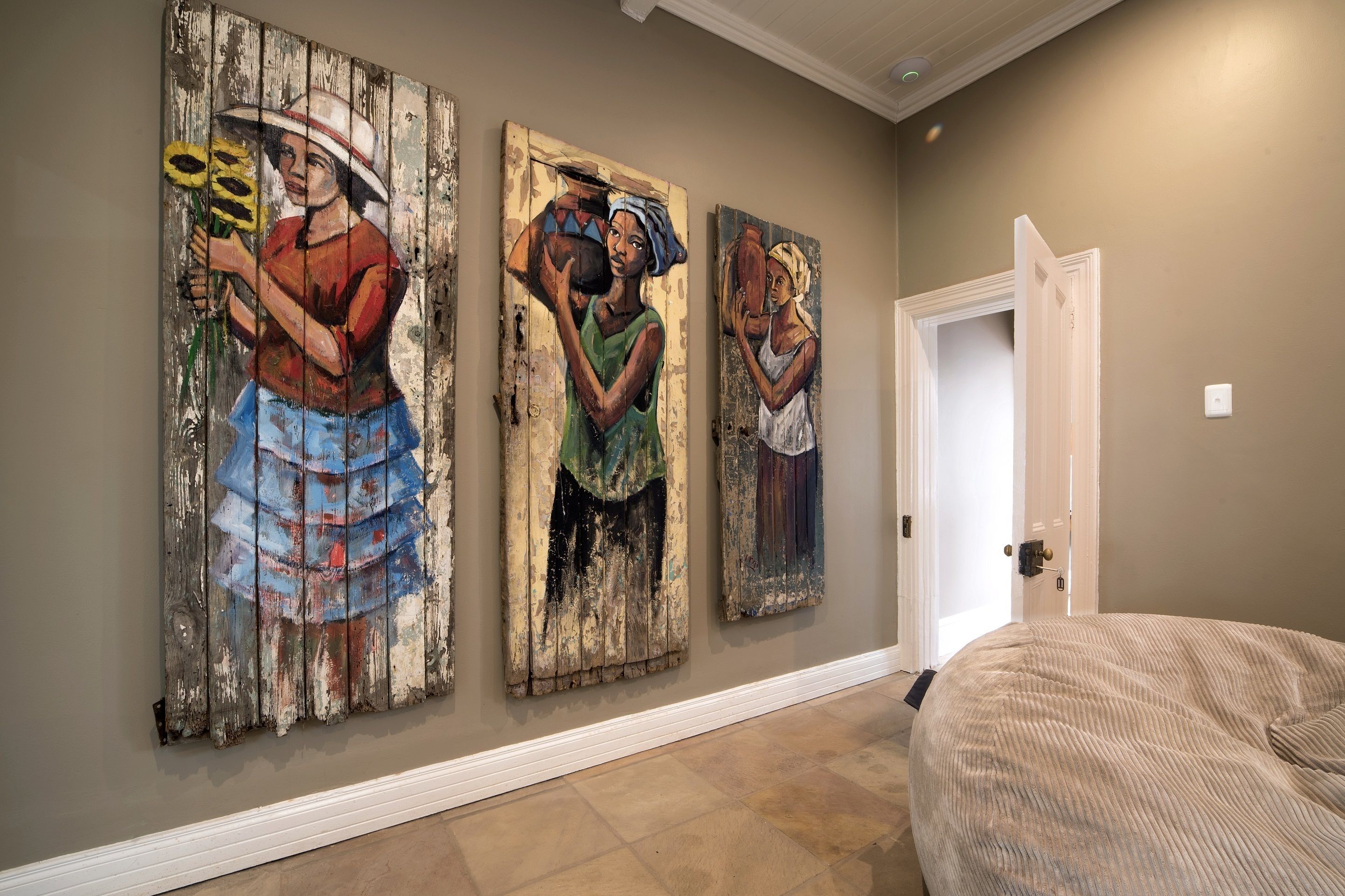 A hallway with three rustic paintings on the wall, a white door, and a beige bean bag chair.