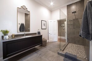 A modern bathroom with a dark vanity, a large mirror, a shower with glass doors, and a tiled floor.