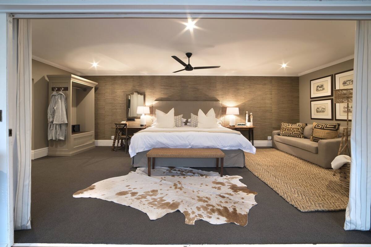 A bedroom with a large bed, a ceiling fan, a nightstand, a sofa, and a rug.