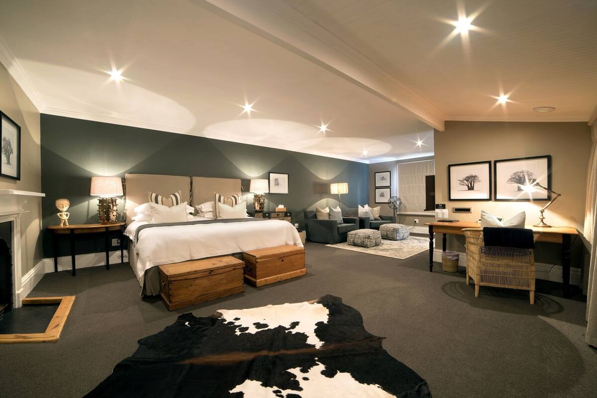 A spacious bedroom with a large bed, a desk, and a chair, along with a fireplace and a cowhide rug.