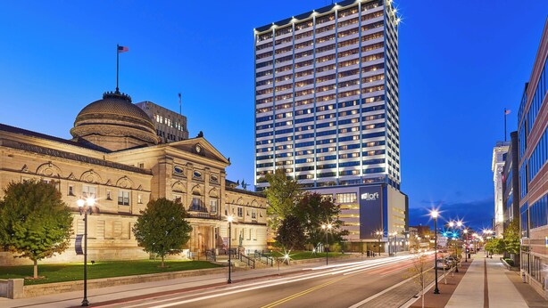 Un bâtiment historique surmonté d’un dôme et un hôtel moderne, une tour imposante dont les fenêtres sont illuminées.