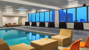 Une chambre d’hôtel avec piscine, coin salon et grandes fenêtres donnant sur la ville.