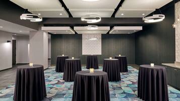 A conference room with round tables covered in black tablecloths, each with a candle. The room has a modern ceiling design with circular light fixtures and recessed lighting.