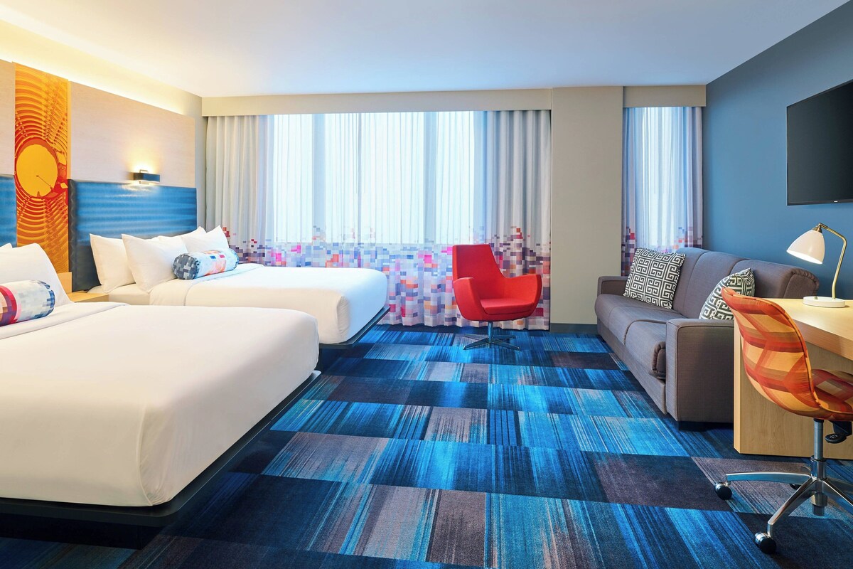 A hotel room with two beds, a sofa, a desk, and a chair.
