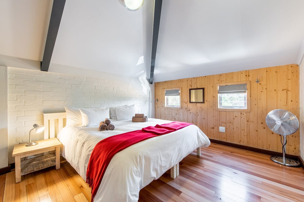 A bedroom with a bed, bedside table, lamp, and a standing fan.