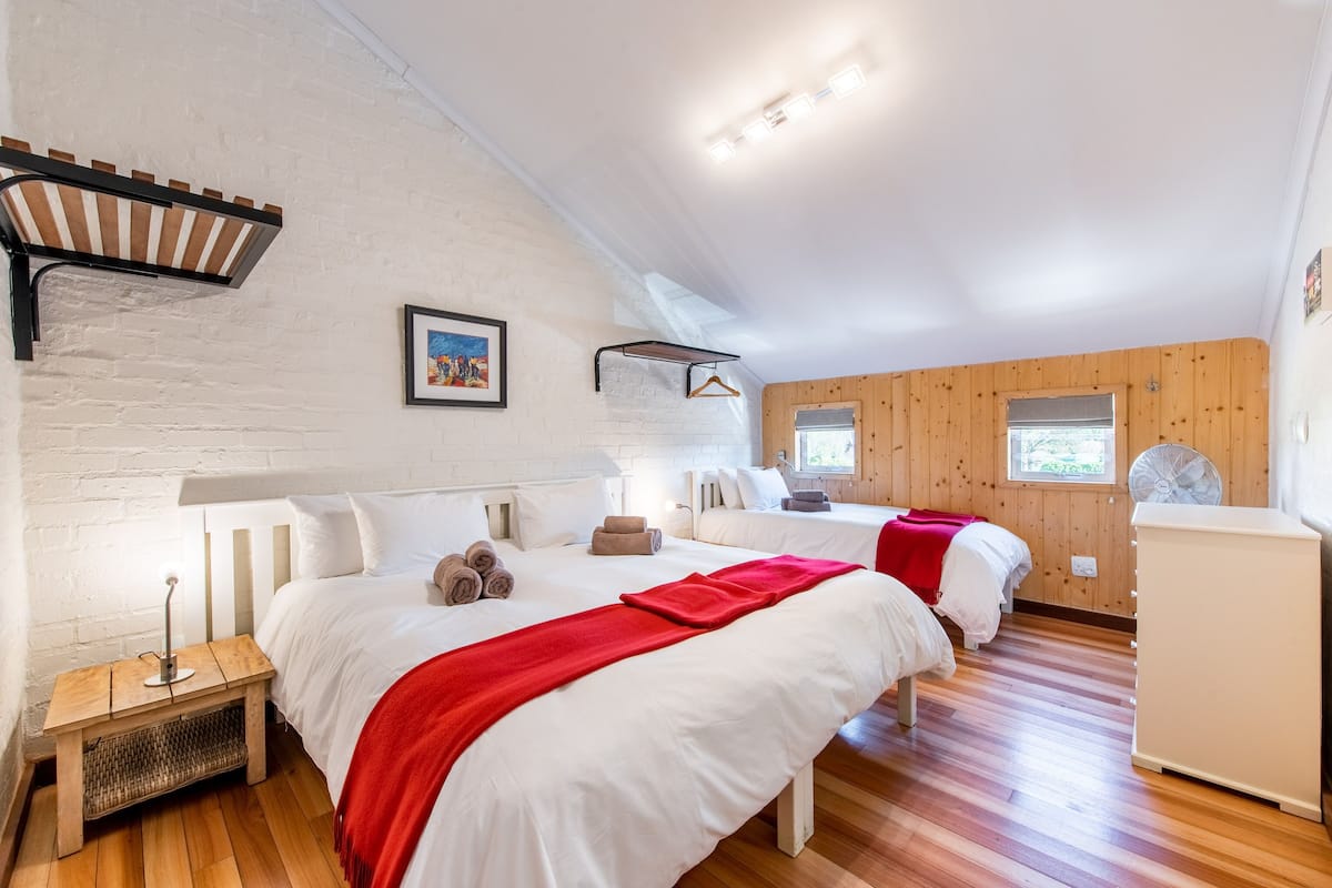 A bedroom with two beds, a wooden bench, a small table, and a fan.