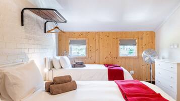 Une chambre d’hôtel avec deux lits, un mur en bois, une fenêtre, un ventilateur et une commode blanche.