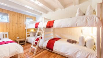 Three comfortable beds with white bedding and throw blankets, a small table, and a window with a view of the surrounding trees.