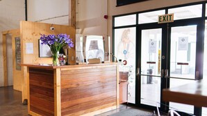 A reception desk with a wooden finish, a vase with purple flowers, and a sign indicating an exit. - Trails End Bike Hotel (Grabouw)