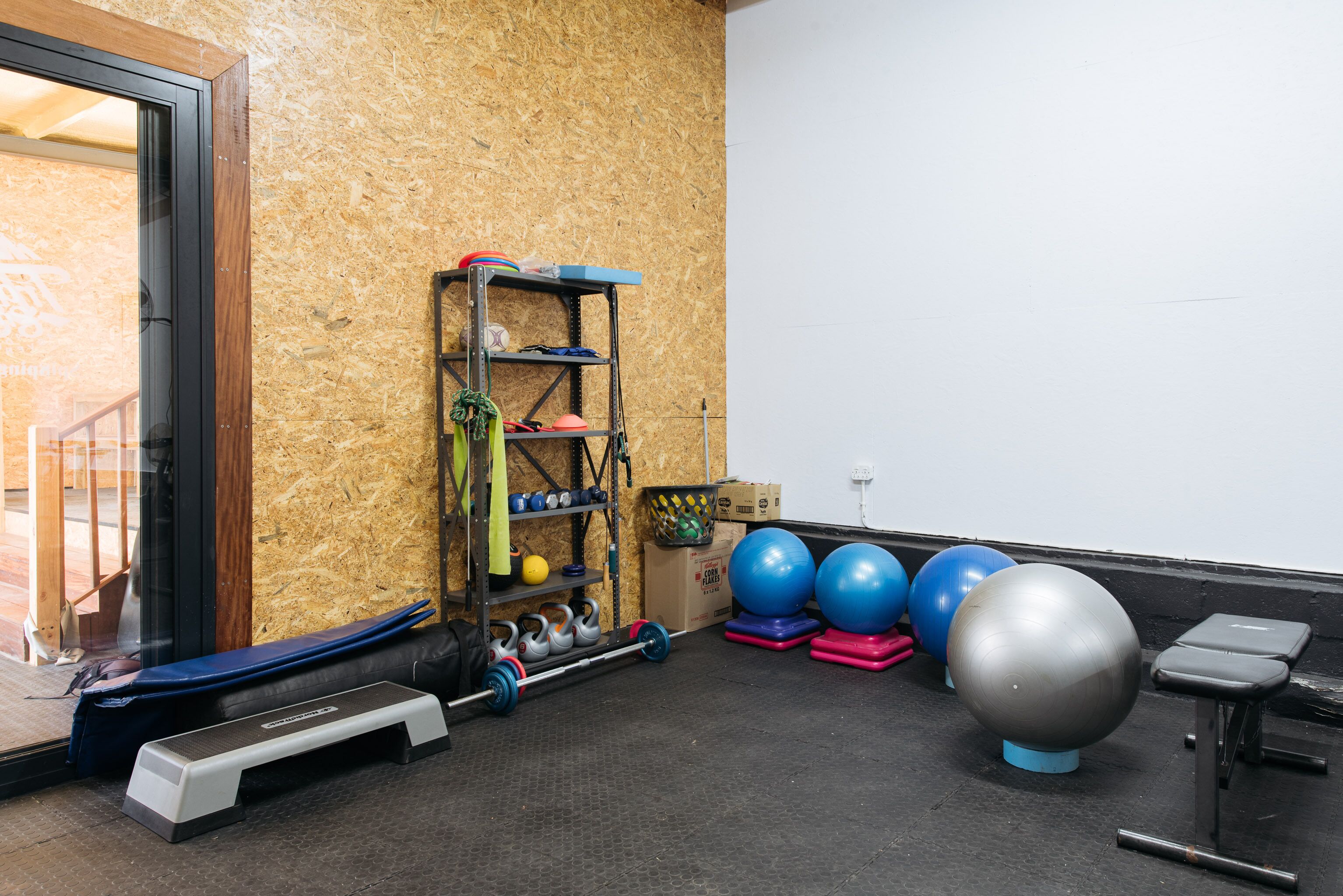 Una palestra con attrezzature per esercizi, una pedana rialzata e uno scaffale a parete con diversi oggetti.