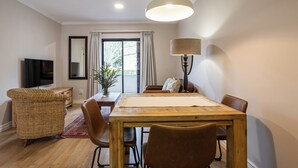 Un coin repas avec une table en bois, des chaises marron, un fauteuil en osier, une lampe et un téléviseur.