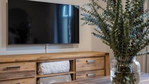 Un salon moderne avec un téléviseur à écran plat fixé au mur, des meubles en bois et un vase orné de feuillage vert.