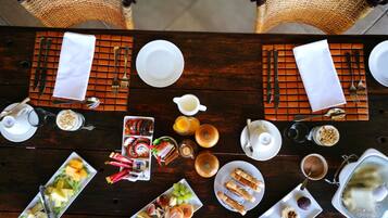 A dining table set with various dishes, including fruits, pastries, and beverages, surrounded by wicker chairs.