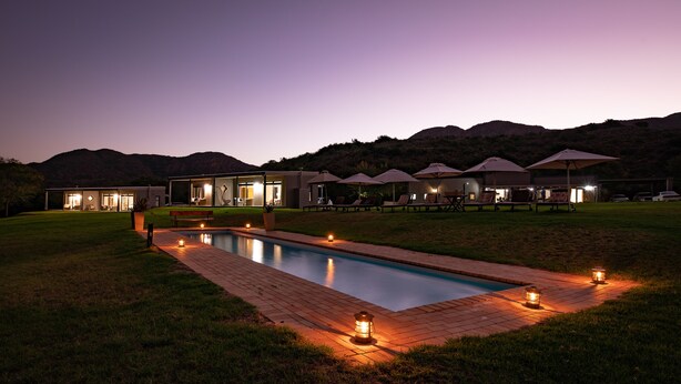 A modern resort with a swimming pool, outdoor seating, and a mountain backdrop. - Wildehondekloof (Oudtshoorn)