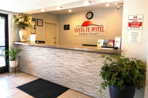 A reception desk at Santa Fe Motel with a clock, a sign, and a potted plant.