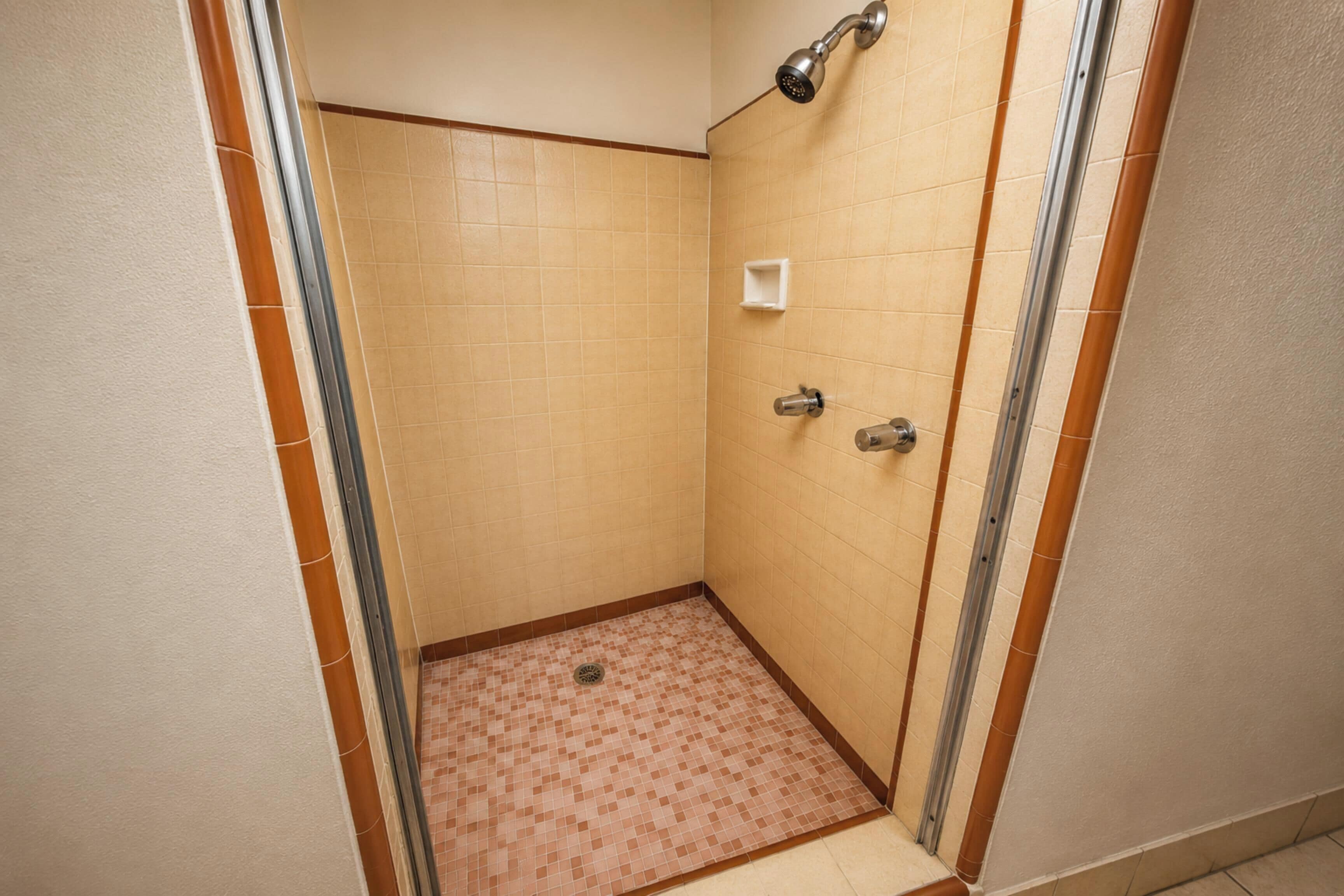 A small, enclosed shower area with tiled walls and floor, a showerhead, and a handrail.
