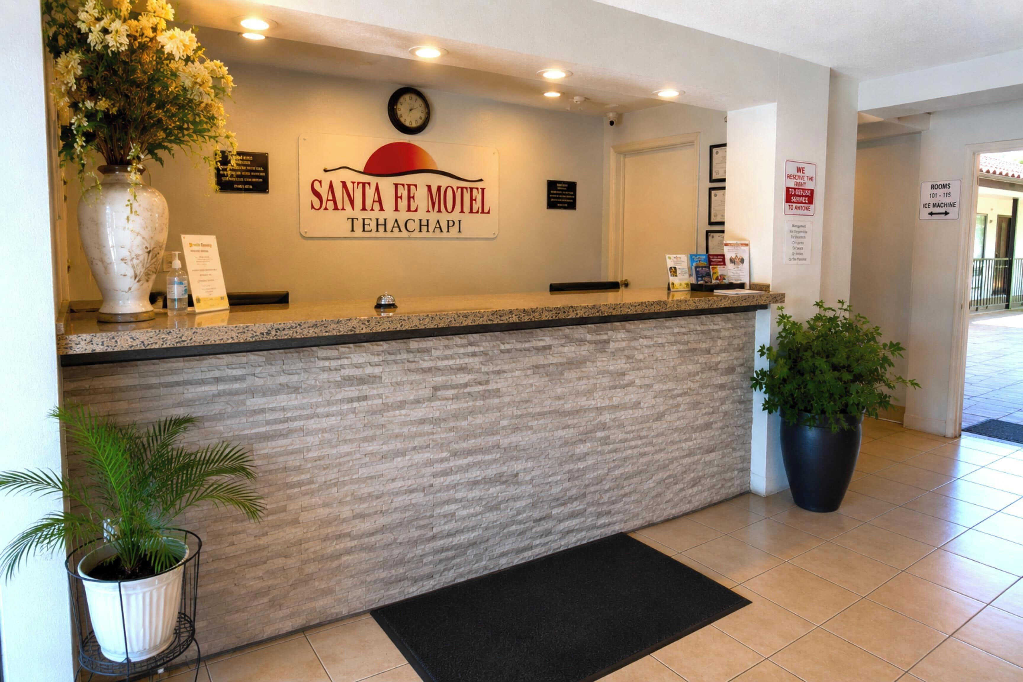 Una mesa de recepción en Santa Fe Motel, con un reloj, un cartel y una planta en maceta.