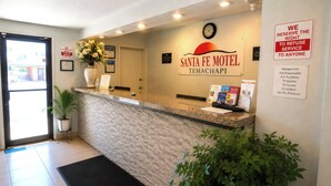 Un comptoir d’accueil dans le motel Santa Fe, avec une horloge, un panneau indicateur et une plante en pot.